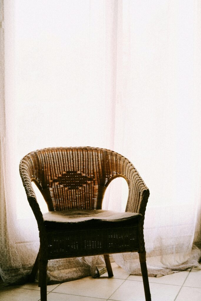 A rattan chair placed beside sheer curtains, with a warm and inviting ambiance.