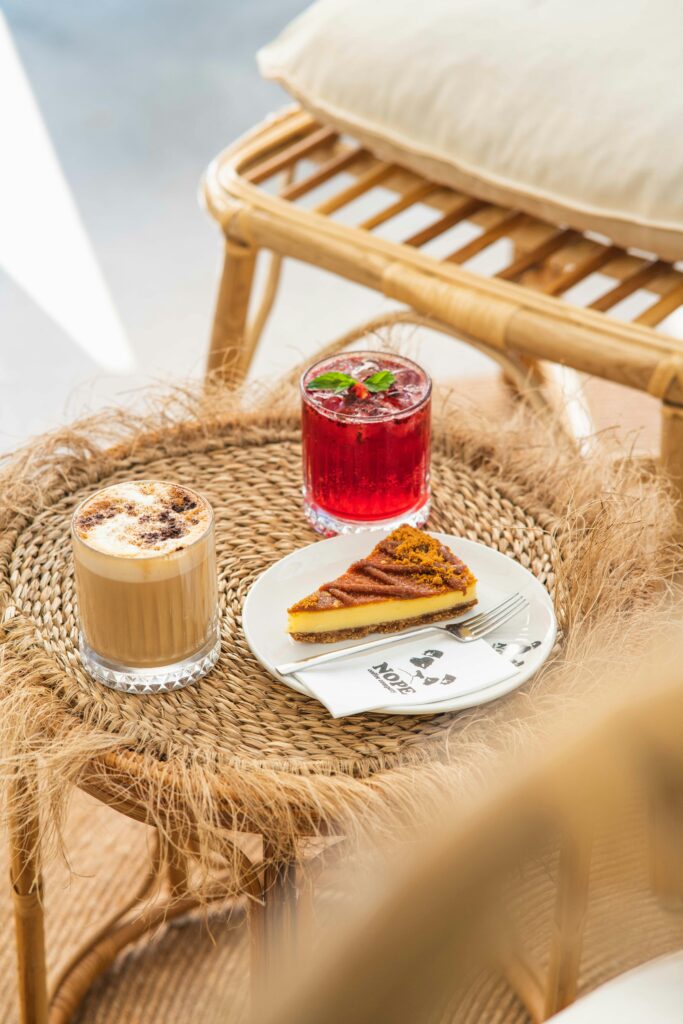 Inviting cafe scene with coffee, red drink, and slice of pie on a rattan table.